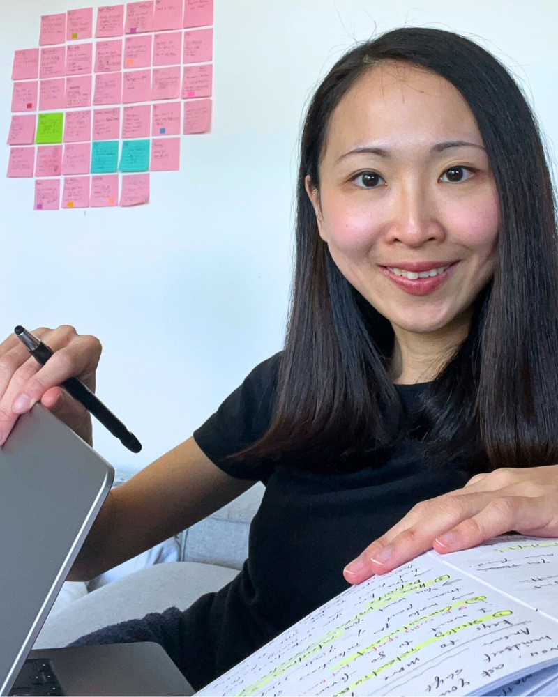 Grace Leung working at her desk with a stylus, laptop and handwritten notes
